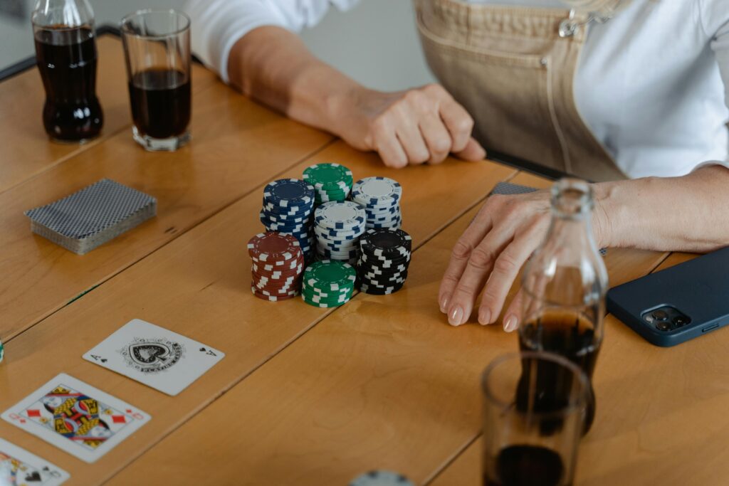 People playing poker with cards and chips on a wooden table, enjoying drinks.